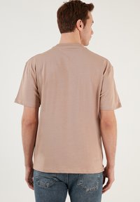 Beige pamut póló rövid ujjal, kerek nyakkivágással és laza szabással, világoskék farmernadrággal párosítva.