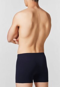 Boxer shorts in cotone blu navy scuro con un design aderente, dal tessuto morbido e con cintura elastica, mostrati di schiena su un torso nudo.