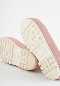Chaussures avec semelles en caoutchouc beige et partie supérieure en textile rose texturé, présentant un motif de semelle rugueux et des détails renforcés au niveau du talon.