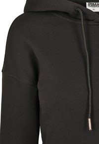 Hoodie noir en coton biologique avec une coupe décontractée, doté d'une capuche avec cordon de serrage, de poignets côtelés et d'une étiquette portant "URBAN CLASSICS."