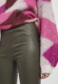 Maglione lavorato a maglia oversize rosa e bianco con un tessuto morbido, abbinato a pantaloni in ecopelle verde oliva a vita alta con cuciture laterali.