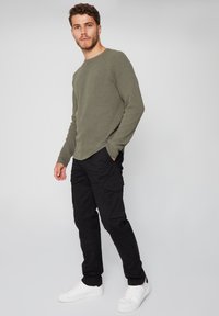 Zielono-oliwkowy sweter prążkowany, czarne spodnie cargo z bocznymi kieszeniami oraz białe niskie sneakersy. Casualowy strój o luźnym kroju.
