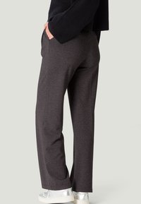 Pantalons gris texturé à taille haute et larges avec poches latérales. Portés avec des baskets argentées, vus de dos.