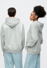 Grå hettegensere med avslappet passform, med kengurulommer og ribbede mansjetter. Kombinert med lyseblå vide jeans.