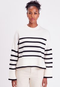 Pull blanc avec des rayures horizontales noires, manches et ourlet côtelés, avec un col rond et une coupe décontractée. Texture douce, design casual.