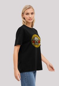 Black t-shirt with a round graphic featuring yellow and red accents, depicting a skull surrounded by roses, made from cotton fabric.