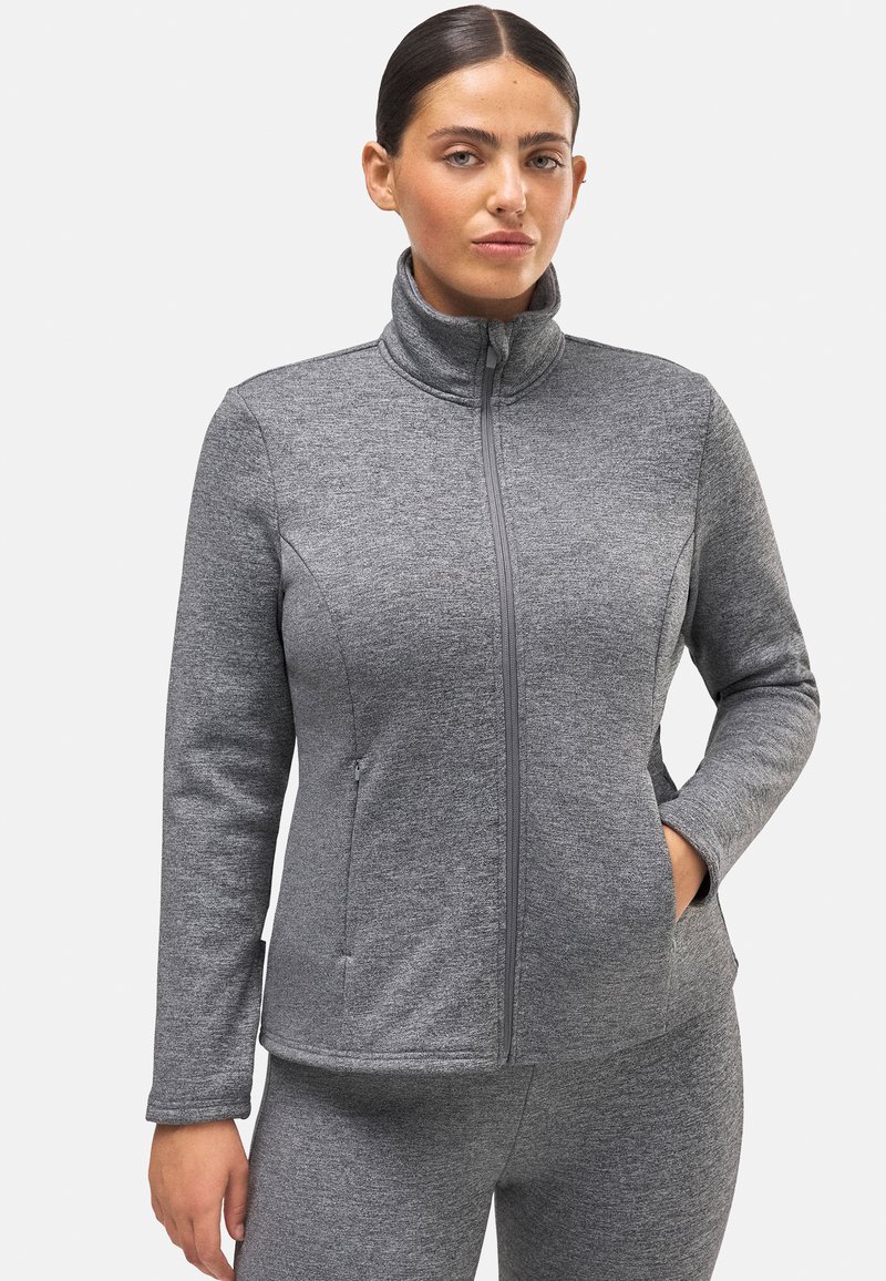 Chaqueta gris con cremallera, cuello alto, mangas largas y bolsillos laterales. La tela tiene una apariencia suave y texturizada con un diseño ajustado.
