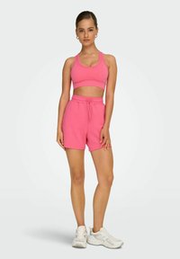 Rosa sportlicher Crop-Top und passende Shorts mit einem elastischen Bund, aus einem weichen Material. Weiße Sneaker mit Schnürdetails.