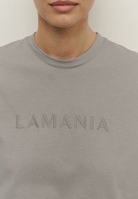 Szara bluza z haftowanym napisem "LAMANIA" na klatce piersiowej. Materiał wygląda na miękki o gładkiej fakturze, z klasycznym okrągłym dekoltem.
