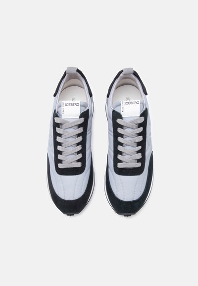 Ζευγάρι λευκών και μαύρων αθλητικών παπουτσιών με γκρι κορδόνια, σε θέαση από ψηλά, με ετικέτα της μάρκας "ICEBERG" στη γλώσσα.