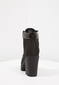 Black suede ankle boot with a glossy black accent at the top, chunky heel, and textured sole. Minimalist design, versatile style.