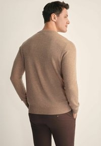 Brązowy sweter dzianinowy z okrągłym dekoltem, charakteryzujący się gładką teksturą oraz ściągaczami przy mankietach i u dołu, zestawiony z ciemnobrązowymi spodniami.