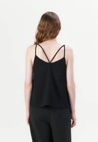 Haut noir sans manches à coupe ample, avec des fines bretelles et un dos en forme de V. Confectionné dans un tissu léger.