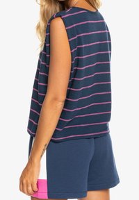 Mörkblå randig topp med rosa linjer, avslappnad passform, vida ärmhål. Kombinerad med mörkblå shorts med rosa och vita detaljer på sidan.