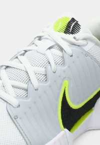 Αθλητικά sneakers με λευκό πλέγμα επάνω, μαύρες και νεονκίτρινες λεπτομέρειες, υφή στη σόλα και παραδοσιακό σύστημα κορδονιών.