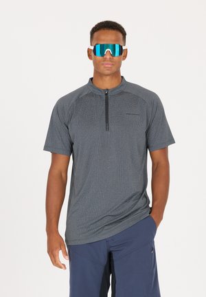 Kurzärmliges, graues Sportshirt mit halbem Reißverschluss und Kragen, kombiniert mit großen, bläulich getönten Sonnenbrillen. Glatte Textur, leichtes Material.