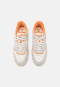 Białe i szare sneakersy z pomarańczowymi akcentami, z teksturowaną zamszową cholewką, perforowanym noskiem i płaskimi sznurówkami. Logo na języku.