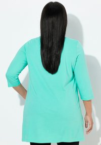 Una lunga camicia verde menta con maniche a tre quarti, realizzata in un tessuto liscio, con scollo arrotondato e vestibilità comoda.