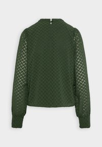 Blouse verte à manches longues, en tissu texturé avec un motif géométrique, col rond avec une ouverture en forme de clé à l'arrière.