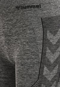 Šedé sportovní legíny vyrobené z texturované tkaniny, se černým logem a cikcakovým vzorem na straně pro jedinečný design.