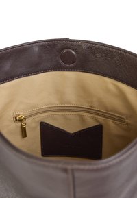Intérieur de sac à main en cuir marron avec une texture lisse, doté d'une poche zippée en or, d'une doublure beige et d'une étiquette en cuir foncé avec une découpe triangulaire.