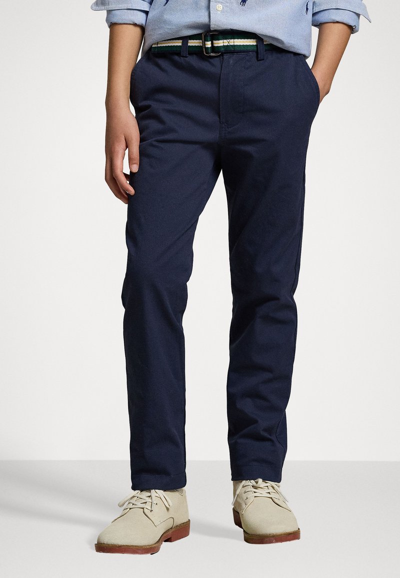 Chino navy con tasche laterali, vestibilità slim e cintura a righe verdi. Presenta una texture liscia ed è abbinato a scarpe chiare.