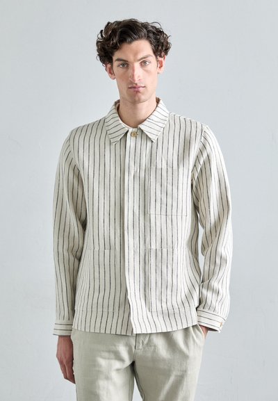 Veste en coton crème légère avec des rayures verticales navy, un col, deux poches avant et une fermeture à boutons.