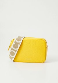 Borsa a tracolla rettangolare gialla con texture, con tracolla beige e bianca a motivo, appoggiata su uno sfondo bianco.