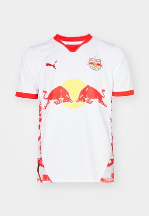 Fehér foci mez piros kiegészítőkkel, kerek nyakkal, Red Bull logóval és oldalsó mintákkal. Könnyű anyagból készült.