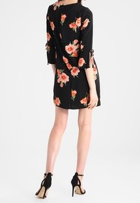 Czarna sukienka w kwiaty z rękawami o długości trzech czwartych, zdobiona różowymi kwiatami, z wiązaniami przy rękawach oraz z zapięciem na guziki z tyłu. Uzupełniona czarnymi szpilkami.