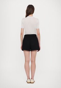 Vit ribbad kortärmad topp, svarta högmidjade shorts och ljusa skor. Fokus på enkelhet och rena linjer i designen.