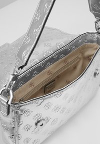 Silberne prägte Handtasche mit strukturierter Oberfläche, verstellbarem Schultergurt und einem mit beigem Stoff gefütterten Reißverschluss-Innenfach.