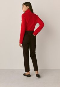 Pulover roșu cu guler înalt, asortat cu blugi negri cu talie înaltă și balerini negri. Textură fină, design ajustat și manșete cu ritm.