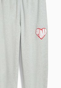 Pantalones de chándal grises hechos de una tela suave, con un gran logo de corazón rojo que lleva el texto "PUMA" en blanco en la pierna izquierda.