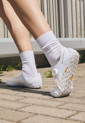 Weiße Merrell-Schuhe mit einer strukturierten Sohle, ausgestattet mit einem BOA-Drehverschluss und einem perforierten Mesh-Obermaterial, getragen mit weißen Socken.