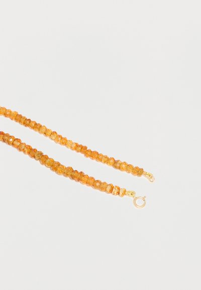 Collier à double rangée de perles ambrées avec fermoir rond en or sur fond blanc.