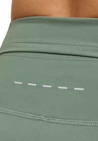 Leggings verdi a vita alta con una finitura liscia, cuciture piatte e una fila decorativa di linee orizzontali bianche sul retro.