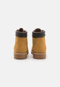 Bottines en daim marron avec un col replié noir, semelles en caoutchouc et détails de couture visibles. Design simple, construction robuste.