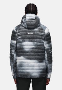 Giacca imbottita in tonalità grigie e bianche con cappuccio, caratterizzata da un motivo a gradiente, strisce orizzontali e un logo Mammut sulla parte posteriore.