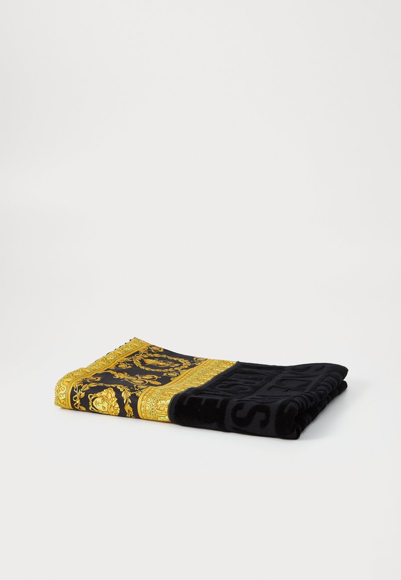 Schwarzes Handtuch mit einem detaillierten goldenen Randmuster. Das Material scheint weich mit einer plüschigen Textur zu sein. Das Design umfasst ornamentale Motive und fette Schriftzüge.