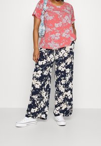 T-shirt floral en corail à manches courtes, associé à un pantalon large marine avec un motif floral blanc. Baskets en toile blanches.
