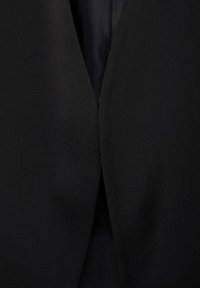 Blazer nero con una texture liscia e opaca. Presenta un profondo scollo a V e un design minimalista senza chiusure visibili o decorazioni.
