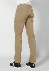 Jeans beige ajustados con una textura suave, diseño de cinco bolsillos y costuras en contraste. Llevados con zapatillas negras de suela plana.