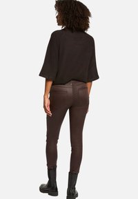Top nero a maniche corte abbinato a pantaloni marroni aderenti con dettagli in borchie e tasche laterali. Stivali neri completano il look.