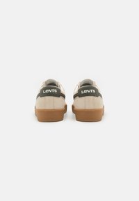 Levi's sportcipő bézs suede felsőrésszel, zöld bőr részletekkel és barna gumitalppal. A saroknál logóval és texturált hátsó résszel rendelkezik.