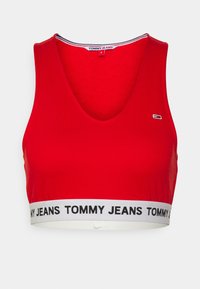 Raudonas medvilnės trumpas viršus su giliu V iškirpte. Yra balta juosta su užrašu "TOMMY JEANS" juodu spalva. Lygus paviršius, sportiškas dizainas.