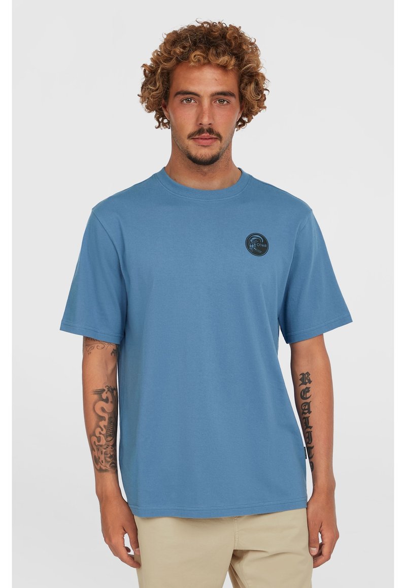 Light blue cotton t-shirt with short sleeves, round neck, and a circular black logo on the left chest. Features a relaxed fit.