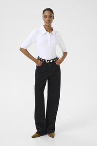 Hvit stripete polo med krage og knappeplacket, kombinert med høyt liv sorte jeans, aksentuert av et svart belte med metalliske sirkulære detaljer og spissede gule sko.