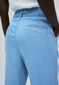 Los pantalones de mezclilla azul claro tienen una cintura alta con una textura suave, dos bolsillos traseros y un diseño de corte relajado.