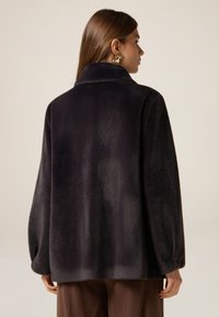 Abrigo de piel negra de gran tamaño con cuello y hombros caídos. Textura suave y diseño minimalista, con un dobladillo recto y sin cierres visibles.
